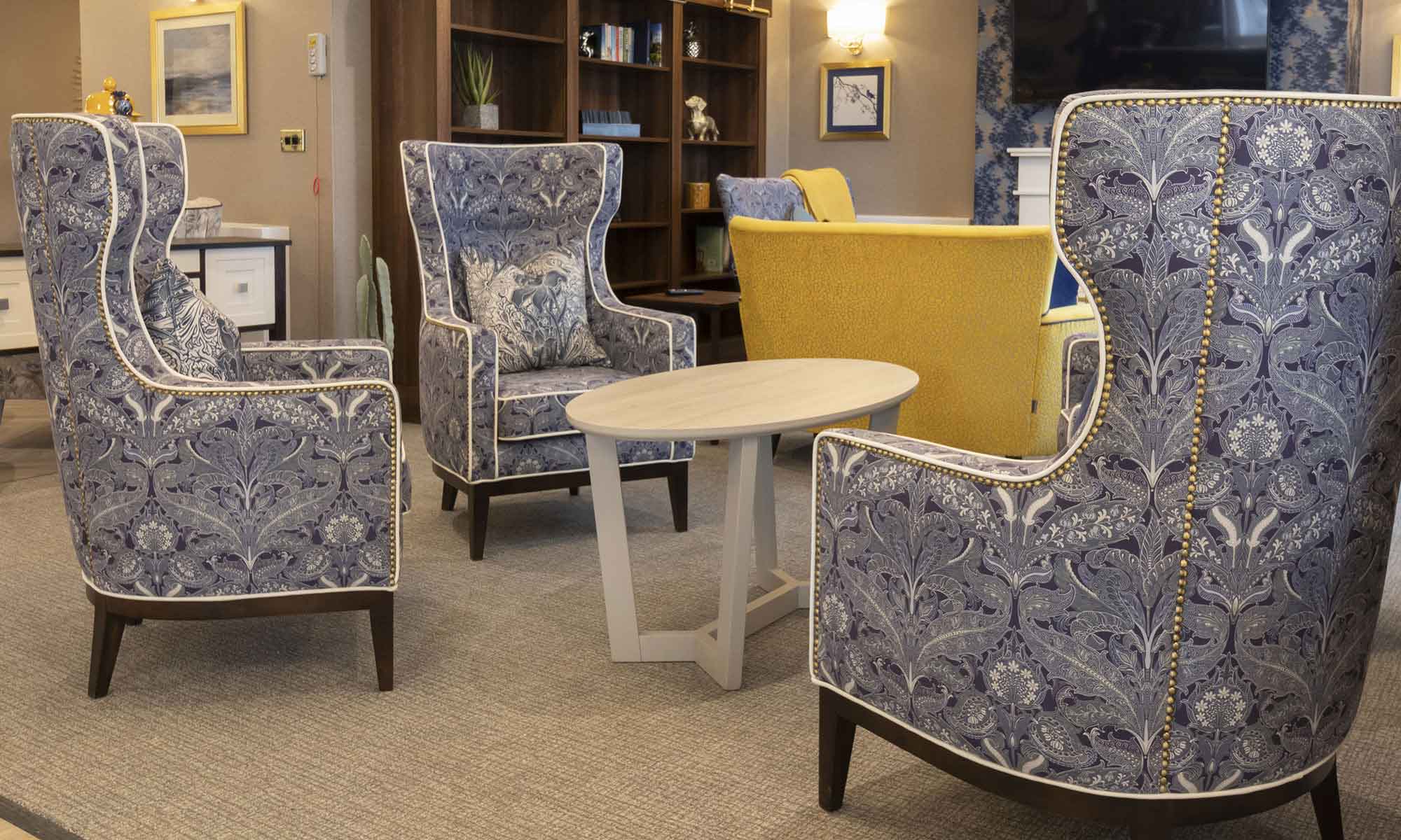 The lounge at St Mary's Care Home with a close up of the Valls wing back chair with gold studding upholstered in a damask heritage pattern fabric.