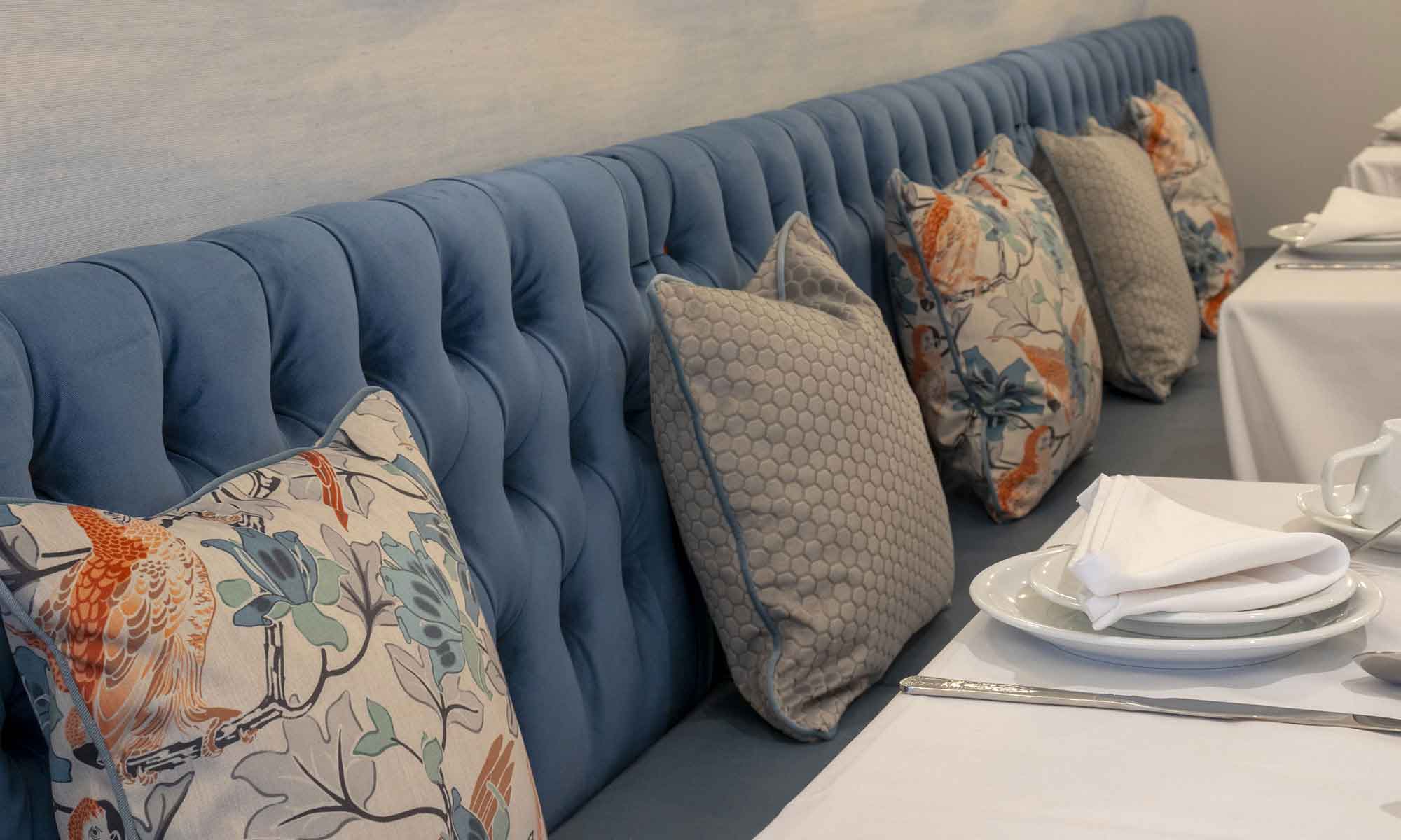 Dining room interior of St Mary's Care Home, a close up of pale blue banquette seating with contrasting scatter cushions.