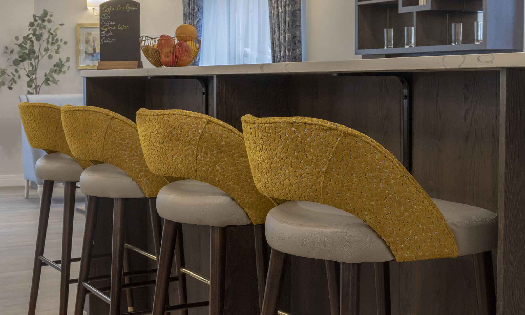 Four Paulo bar stools in a mustard fabric against a walnut bar with marble top