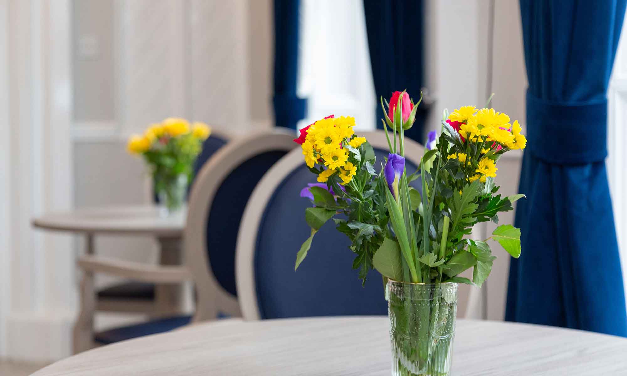 Dining area at Newton House Care Home. Shackletons Stamford Dining Table with Westbourne dining chairs wit a vase of flowers on table top.