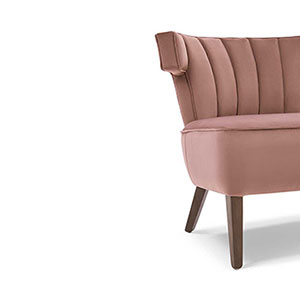 A cropped shot of the Tilton occasional chair showing its T-Shaped design. The Tilton is upholstered in blush pink velvet with dark wood legs