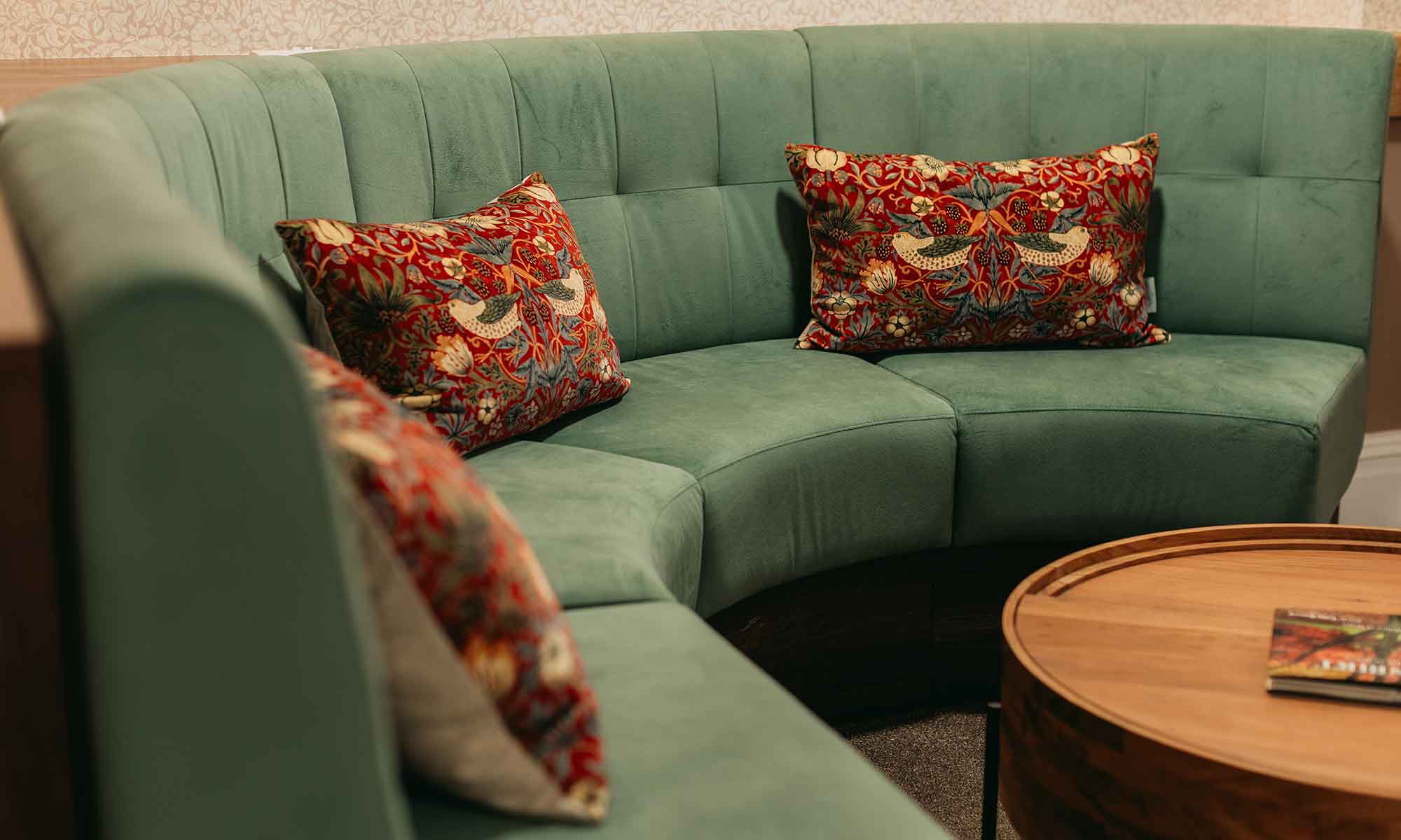 Curved banquette seating in green with cushions and a table