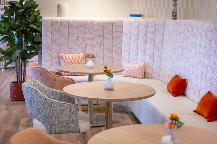 Bespoke banquette seating with upholstered back panels and lounge chairs surrounding circular tables in a calm, welcoming café-style seating area.