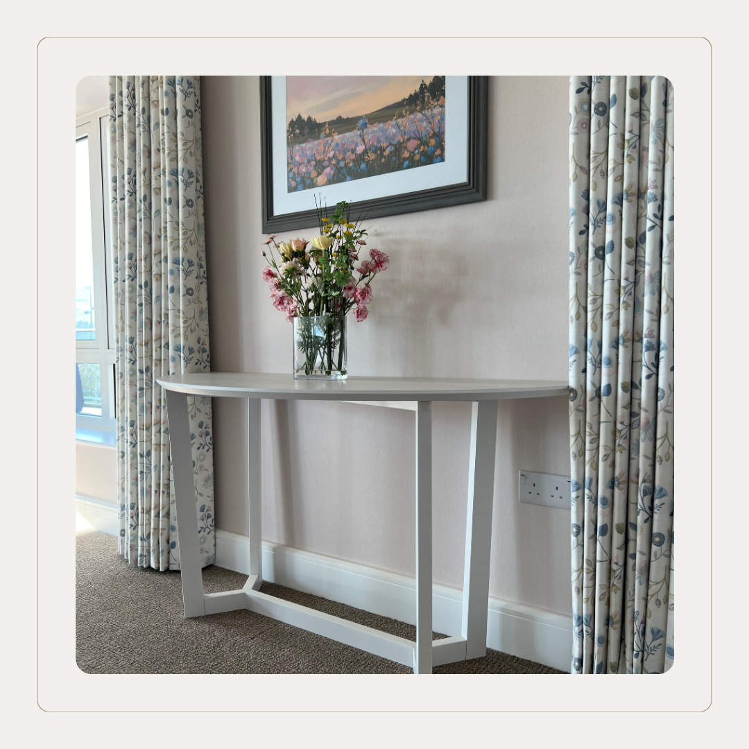Care home console table styled with floral arrangement and soft furnishings in Cloud Dancer inspired neutrals, reflecting Pantone Colour of the Year in senior living interiors.