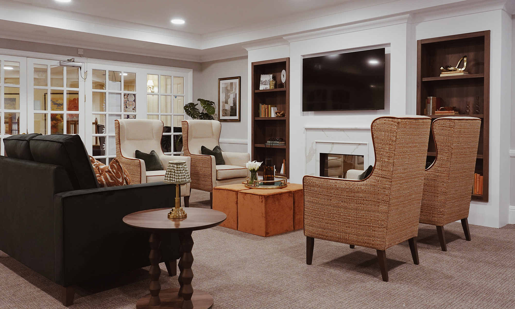 Purley Gardens lounge seating area featuring Shackletons sofa, high back chairs and rust velvet footstools in a warm, luxury care home setting.