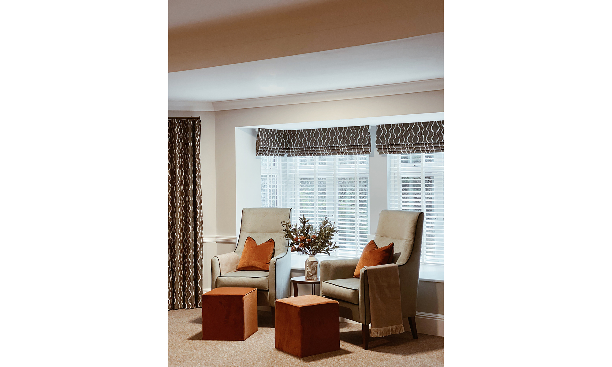 Pair of Denia high back lounge chairs with rust accent cushions and matching velvet footstools by the window at Purley Gardens luxury care home.