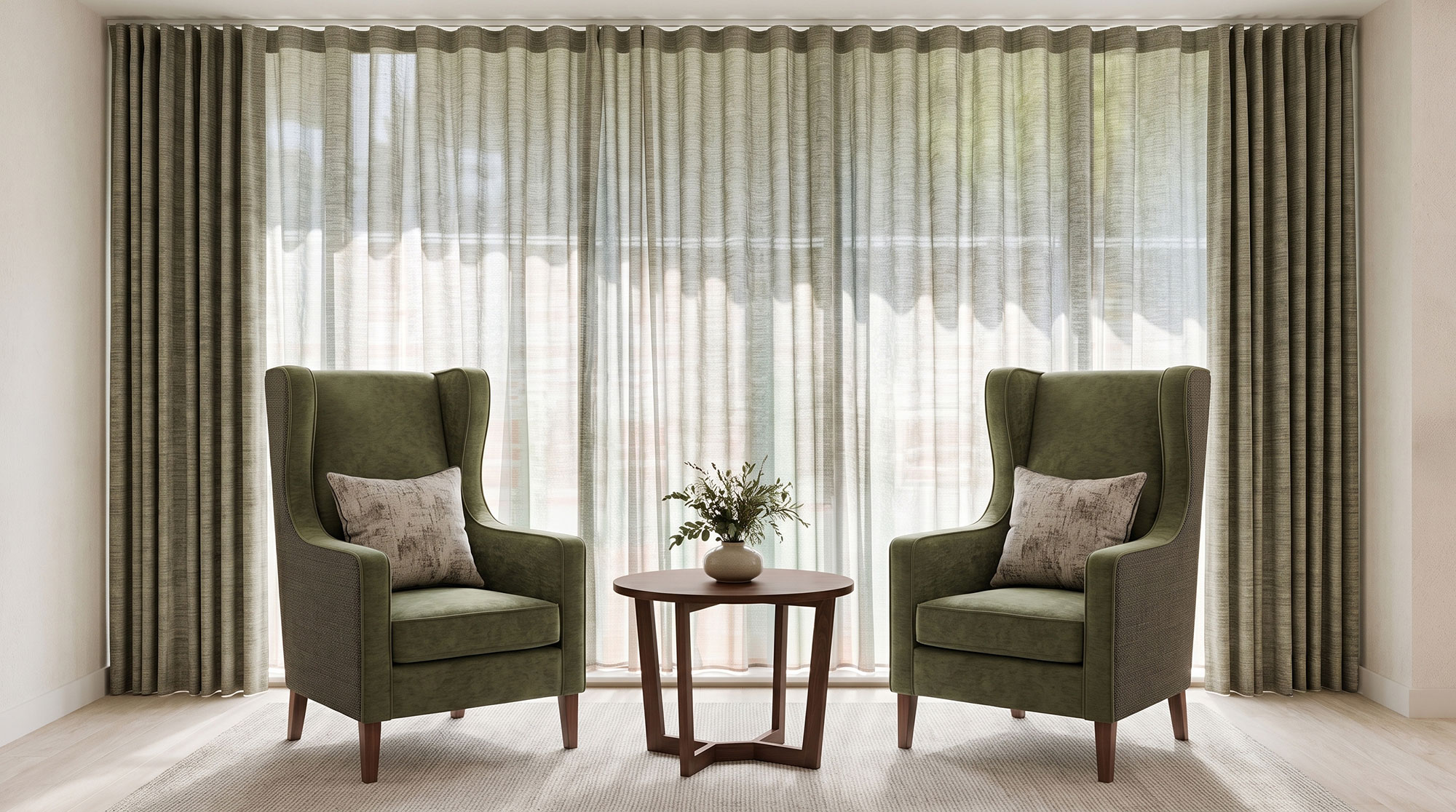 Two green wing-back chairs positioned in front of full-height curtains and sheer voiles.