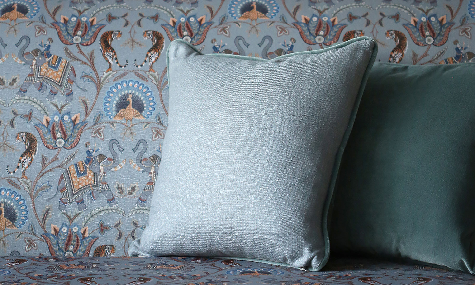 Blue botanical upholstery fabric paired with plain blue piped scatter cushions.