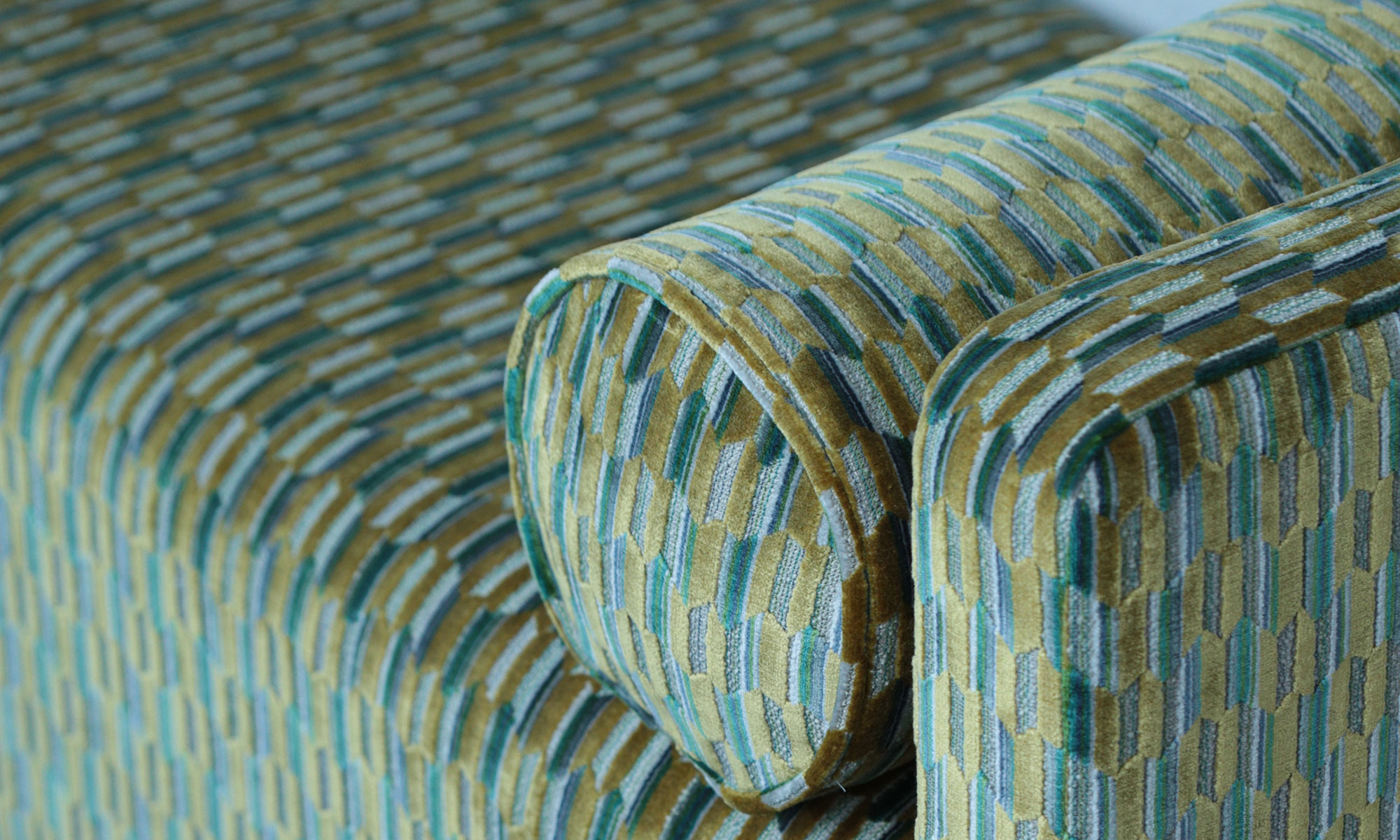 Close-up of patterned green and blue upholstery with a matching cylindrical bolster cushion.