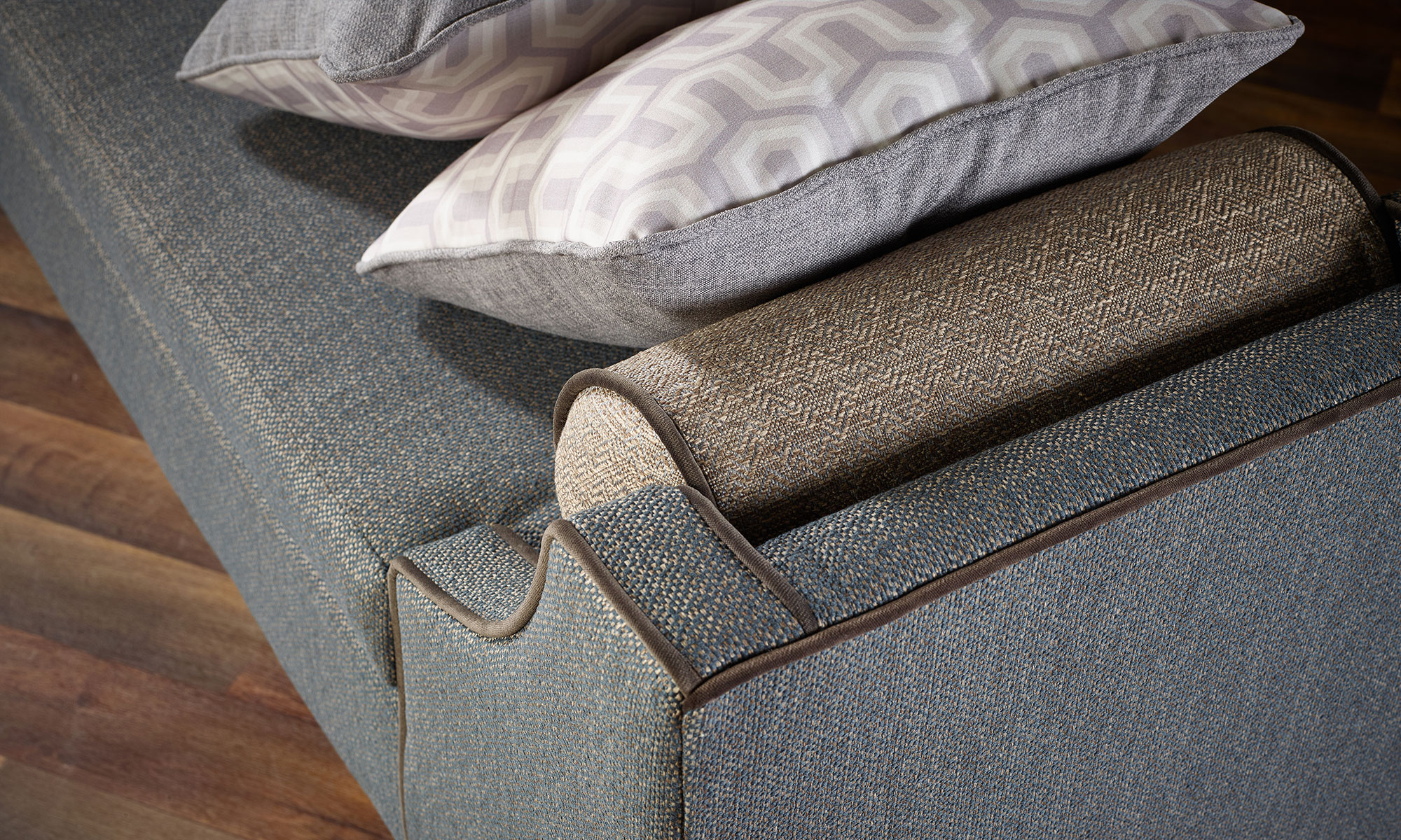 Close-up of a blue upholstered sofa with contrast piping, bolster cushion and patterned scatter cushions.