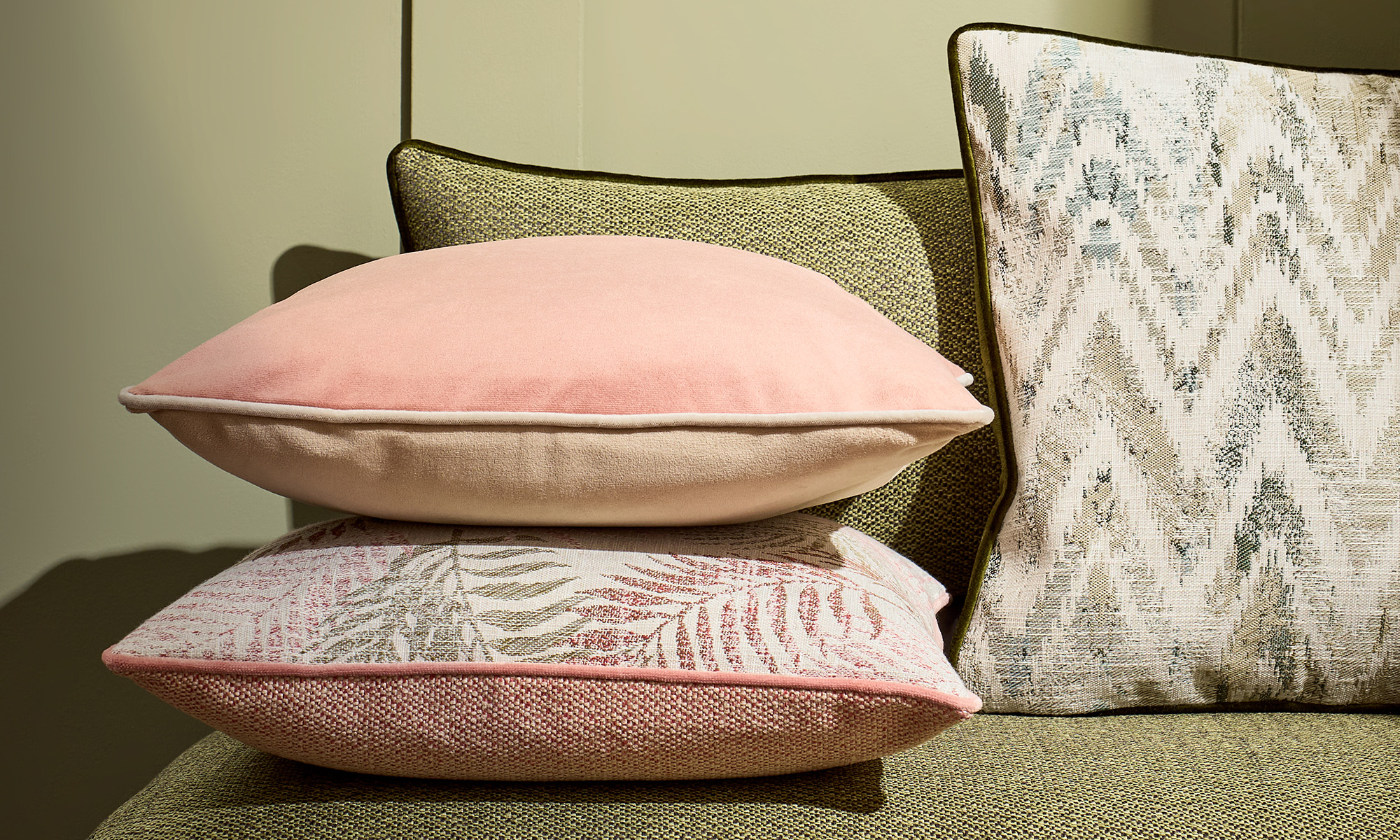 Layered scatter cushions in pink, green and abstract patterned fabrics.