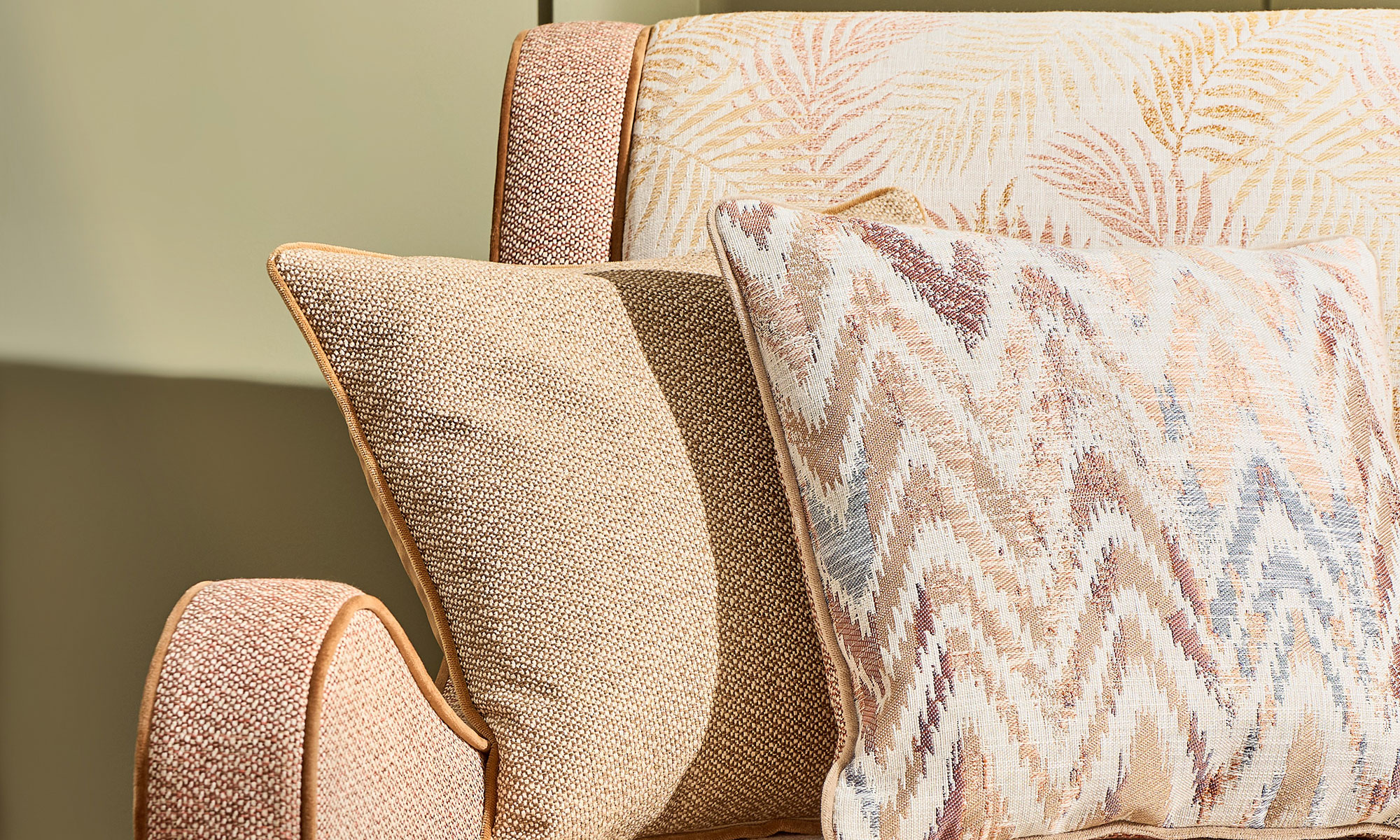 Close-up of an upholstered chair styled with coordinating neutral, coral and patterned cushions.