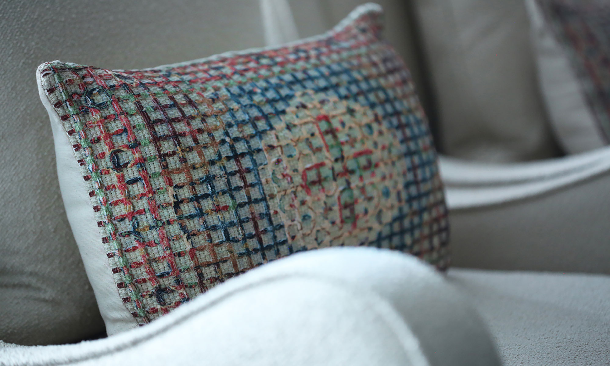 Multicoloured textured scatter cushion displayed on a soft grey upholstered chair.